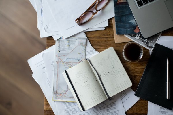 a busy desk in the office filled with books, notes and a cup of coffee